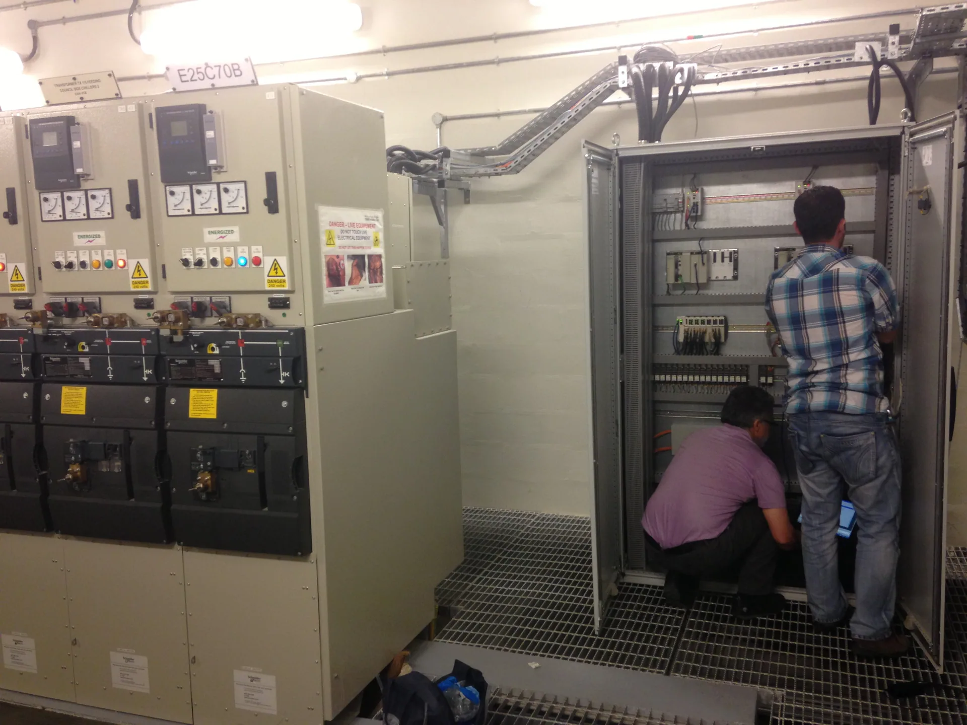 Two engineers working inside a control cabinet next to energised medium voltage switchgear